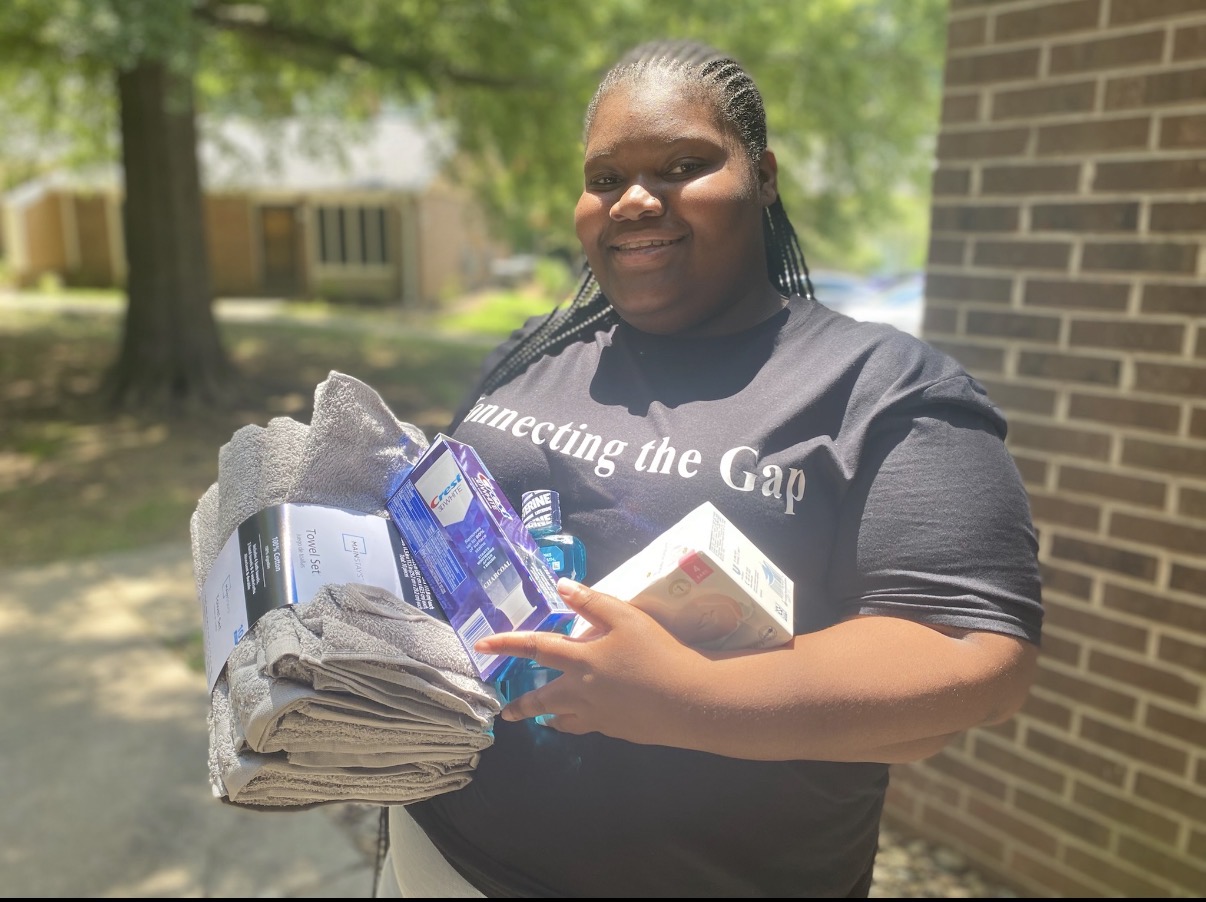 A young volunteer in a Connecting the Gap shirt holding donated towels and toiletries.